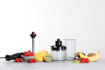 Hand blender kit, fresh fruits and strawberries on gray table against white background, space for...