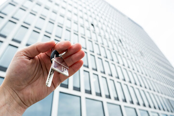 closeup Real estate agent holding key near house outdoors, high-rise buildings of modern city