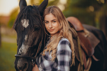A young woman with a horse stands near a fence in autumn at sunset. Breeding thoroughbred horses...