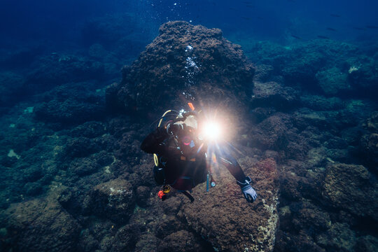 Scuba diver exploring coral reef with flashlight in murky water