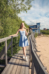 A girl in a blue dress walks by the old pier along the river bank.