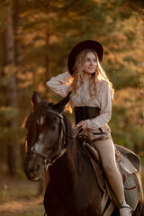 Fototapeta premium A young beautiful woman rides a horse in the forest in autumn. Horseback riding in the evening in autumn.