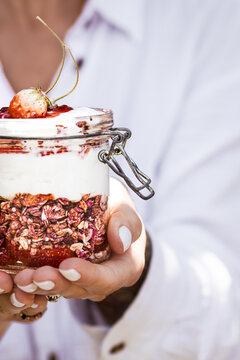 Close-up of a hand holding a jar of yogurt parfait with granola