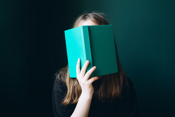 Young girl covering face with book, unrecognizable cropped view