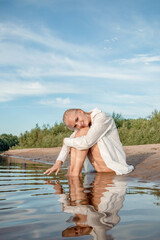 Naklejka premium A girl in a white shirt sits on the shore.