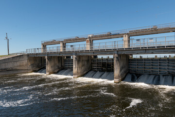 Wide angle shot of a spillway or spill side of a dam with turbulent water and a bright blue sky.