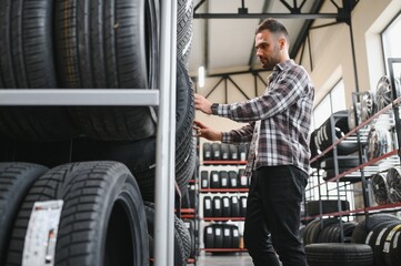 Portrait young man customer examining brand and product characteristics while buying new tires in auto department of dealership.