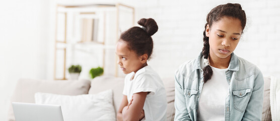 Upset african sisters sitting next to each other on sofa at home, sisters fighting
