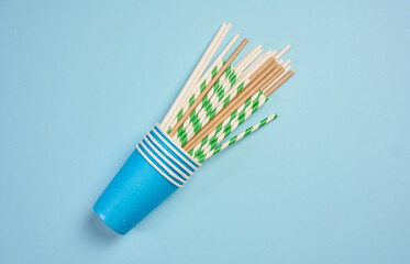 Paper cocktail straws and paper cups on a blue background, top view