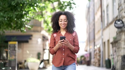 Happy african american young woman tourist walking on city street using smartphone mobile phone Outdoor Smiling black girl female student go browsing internet lifestyle travel trip and journey concept - Powered by Adobe