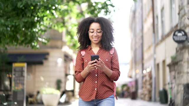 Happy african american young woman tourist walking on city street using smartphone mobile phone Outdoor Smiling black girl female student go browsing internet lifestyle travel trip and journey concept - Powered by Adobe