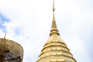 A gold colored pagoda with a gold colored roof. The sky is blue and there are clouds in the sky