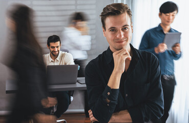 Confidence and happy smiling businessman portrait with blur motion background of his colleague and business team working in office. Office worker teamwork and positive workplace concept. Prudent