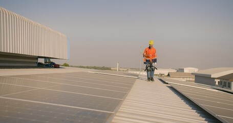 engineer worker in a high-visibility vest walks along a solar panel array on a building roof