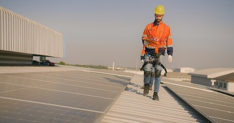 engineer worker in a high-visibility vest walks along a solar panel array on a building roof