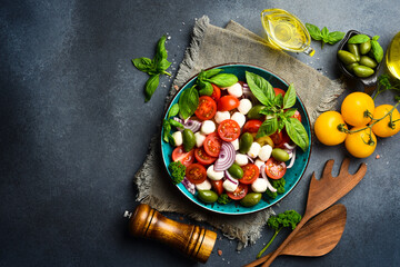 Fresh summer salad: tomatoes, mozzarella cheese, basil and olives. Caprese. On a gray concrete background.