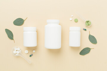 Bottle with pills and green leaves on color background, top view