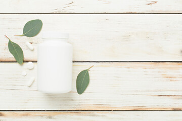 Bottle with pills and green leaves on wooden background, top view