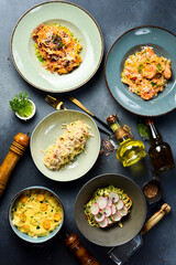 A set of food and dishes on a stone table. A set of pastas with seafood, meat and vegetables. Top view.
