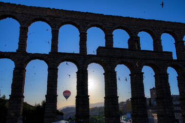 View of the Segovia aqueduct backlit with thousands of swifts and a hot air balloon at dawn. Spain.
