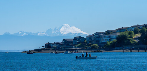 Three men in a fishing boat work on crab pots off Camano Island with community and Mt Baker in background.