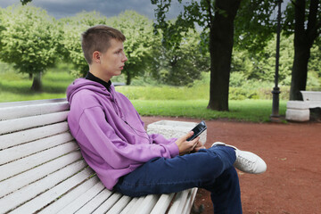 A boy sits on a bench with a phone.