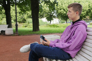 Obraz premium A boy sits on a bench with a phone.