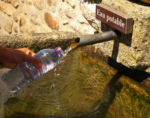 Closeup shot of a hand holding a plastic bottle and filling with drinking water from a spring