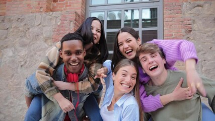 A group of smiling teenagers posing happily for a portrait. Young people laughing and having fun looking at the camera. Guys giving piggyback rides to their female friends. Mates enjoying together