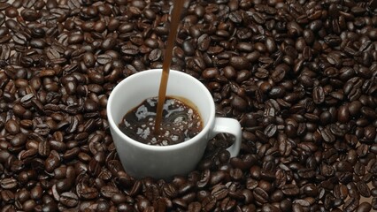 Freshly espresso was poured in white cup with pile of coffee bean. Pouring black coffee in the cup with brown background and seed scattering around on wooden table. Close up. Top view. Comestible.