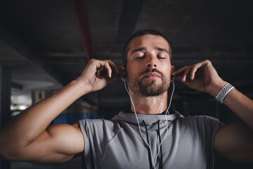 Fitness, music and face of man in garage for commitment, determination or motivation for sport. Male athlete, earphones or eyes closed in parking lot for workout, thinking or favorite song on radio