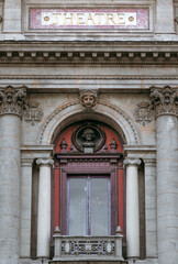 Admiring the exquisite facade of the Lyon Theater, with its tall red-framed windows, intricate stone sculptures, and elegant marble plaque.