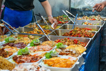 Assorted Thai street food dishes displayed in metal trays at a food stall on Phuket night market. Asian food