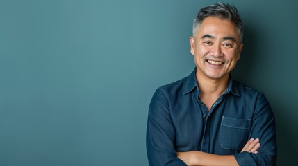 Middleaged East Asian Man Smiling in Casual Denim Shirt, Arms Crossed, Studio Shot, Concept of Happiness and Confidence, Suitable for Professional Use, Soft Blue Background