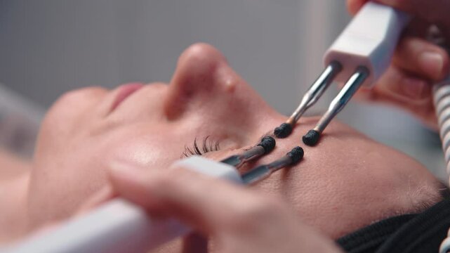 Close-up portrait of a beautiful woman with closed eyes and a skin rejuvenation machine. Salon procedures. Microcurrent therapy