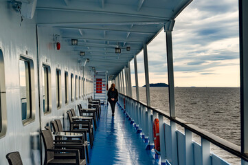 Deck of a ship, lake view, north sea from aboard a cruise ship. Unrecognizable silhouette of a walking and resting woman. The theme of traveling in northern regions and cold water spaces © oksanamedvedeva