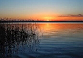 Fototapeta premium serene sunset over the Black Body. The lake reflects an orange and blue sky, with some clouds visible in the distance