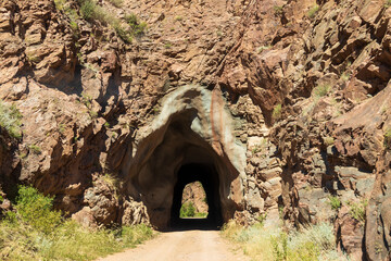 Tunnel on Phantom Canyon Road in the Rocky Mountain in Colorado; old railroad tunnel cut in granite; concepts of adventure, light at end of tunnel, and road less traveled