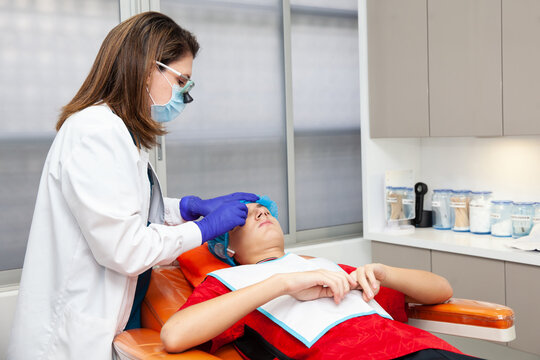 Skin lesion removal procedure. Dermatologist carrying out a removal of benign skin lesion on the face of a young male patient.