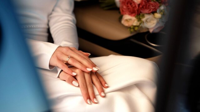 Wedding ring on the hands of a couple. Unrecognizable bride and groom sitting in a car. Beautiful nails of a bride sitting in a car, close-up. - Powered by Adobe