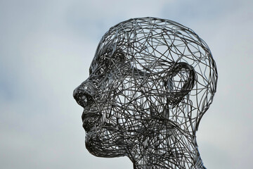 An intricate metal sculpture of a human head standing against a cloudy sky, representing creativity and the complexity of human thought.