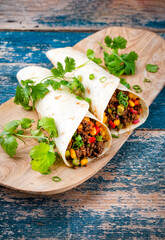 Mexican style burritos - tortilla wrap with spicy minced meat, vegetables and leek served as close-up with hot spices on a wooden chopping board