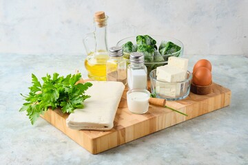 Prepared ingredients for a Greek pie with spinach and feta on a wooden board on a gray concrete background. Spinach recipes.
