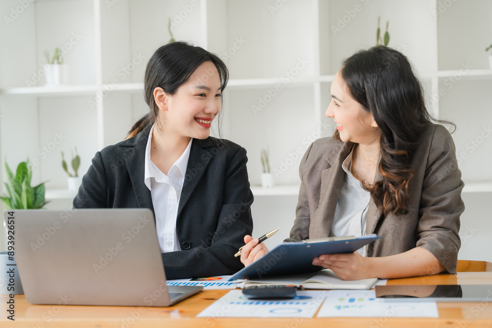 Wall mural collaborative synergy: two young asian businesswomen engage in a productive meeting, their smiles re