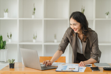 Focused Success: A young Asian businesswoman engrossed in her laptop, radiating productivity and achievement in her modern office space.