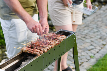 young man grilling meat kebabs on coals, ARROSTICINI - typical southern Italian cuisine, a luxurious picnic on the terrace near the house in summer 