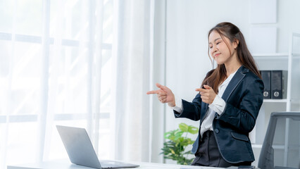 Excited Asian young woman using phone and laptop sitting on a desk office in the day at office