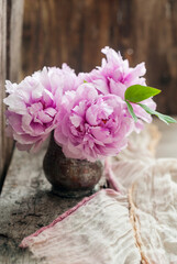Beautiful freshly cut pink peonies in a vintage copper vase on old wooden board with vintage garden scissors and linen runner and copy space