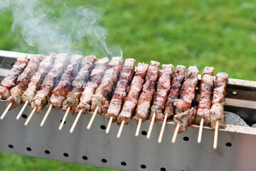 a young man grills meat kebabs on coals, ARROSTICHINI - typical southern Italian cuisine, a luxurious picnic on the terrace near the house in the summer, aromatic smoke rises above the barbecue,