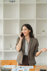 Young charming Asian businesswoman having a phone call with her client while working in the office room.